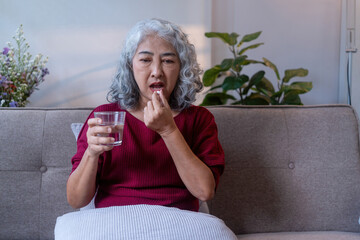 Elderly Woman Taking Pill with Water on Sofa