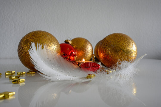 Weihnachtsdekoration auf einem Tisch, Christbaumkugel mit wei&szlig;er Feder und goldenen Sternchen
