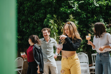 Group of young friends dancing and having fun together while enjoying drinks in an outdoor garden...