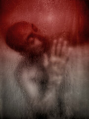 A man behind wet glass, hands pressed against it, expressing emotional pain.