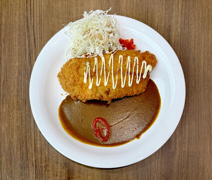 Close up of dori fish curry with Japanese coleslaw and side dish. Served on a white plate, isolated on wooden table.