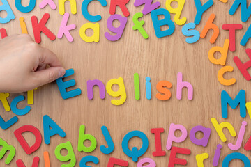 木目のテーブルにカラフルな「English」のアフファベットを並べる手