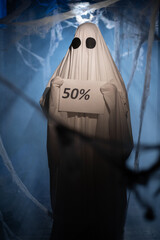 Funny halloween ghost showing paper sign 50 percent discount in dark corridor with many cobweb....