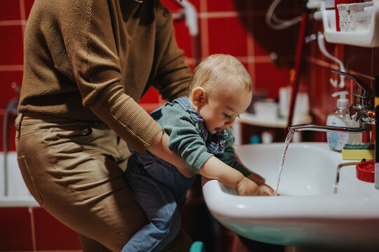 A parent helps their child wash hands in a domestic bathroom, suggesting learning, care, and home routines, with a focus on cleanliness and nurturing family interactions.