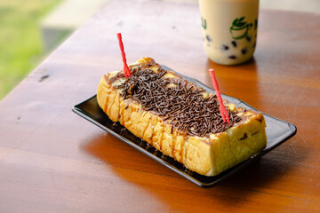 A toasted square bread on a wooden table with an oval black crust and two skewers on each end.
