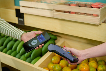 Smartphone held close to card reader during wireless payment at fresh fruit shop contactless...