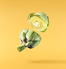 Fresh raw Artichoke falling in the air isolated on yellow background. High resolution image