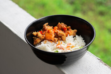 Rice in a black bowl with side dishes of chicken katsu and fresh vegetables
