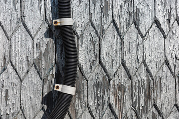 Close up shows weathered wood shingles with peeling paint and a conduit.
