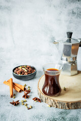 Warm spiced coffee scene: glass cup on wood slice, moka pot, bowl of beans, cinnamon sticks and star-anise on cool grey backdrop - perfect autumn cafe banner