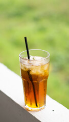 A refreshing glass of iced tea with a black straw, set against a vibrant blurred green background. Perfect for summer, beverages, or outdoor refreshment