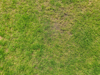 Aerial view of a green grass field highlighting various shades of green, with patches showing wear. Ideal for illustrating landscapes, nature, and outdoor settings.