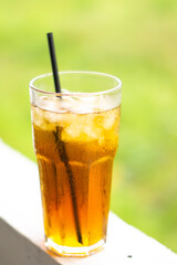 A refreshing glass of iced tea with a black straw, set against a vibrant blurred green background. Perfect for summer, beverages, or outdoor refreshment