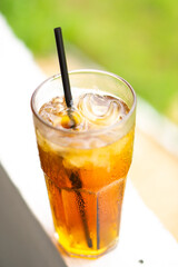 A refreshing glass of iced tea with a black straw, set against a vibrant blurred green background. Perfect for summer, beverages, or outdoor refreshment