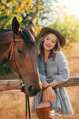 photo real person cowgirl with horse walking on dirt road, field nature summer sky. Woman rider in leather hat holds stallion by reins, sexy Girl blue short dress wild west style. pen, wooden fence