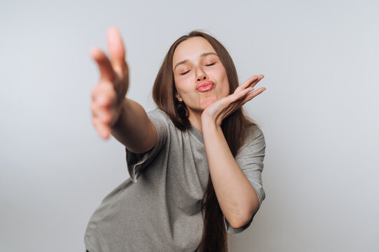 A young woman playfully poses with a kissy face and outstretched arm against a plain background.