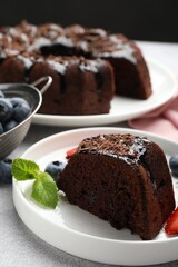 Piece of delicious chocolate bundt cake with mint and blueberries on light grey textured table against black background, closeup