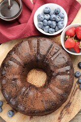 Delicious chocolate bundt cake, strawberries and blueberries on wooden table, flat lay