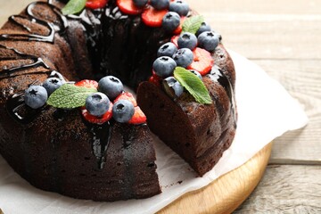 Delicious chocolate bundt cake with strawberries, mint and blueberries on wooden table, closeup