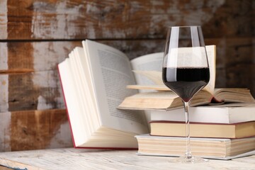 Red wine in glass and books on light table against color wooden background, closeup