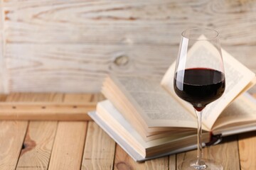 Red wine in glass and book on wooden table against light background, closeup. Space for text