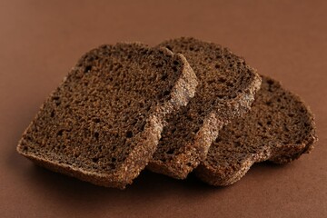 Pieces of fresh rye bread on brown background, closeup