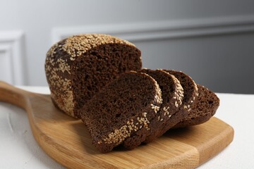 Pieces of fresh rye bread with seeds on white table against light grey wall, closeup