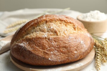 Loaf of fresh bread, flour and spikes on table, closeup