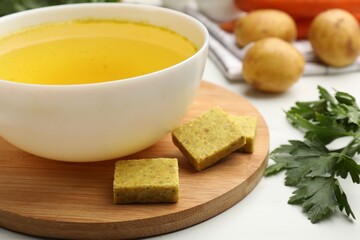 Aromatic bouillon cubes, broth, parsley and vegetables on white table, closeup