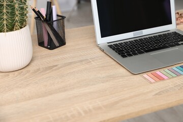 Modern laptop and stationery on wooden desk in office, closeup. Comfortable workplace