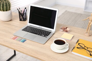Modern laptop, coffee and stationery on wooden desk in office. Comfortable workplace