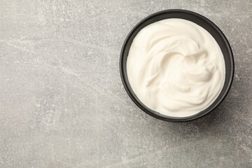 Tasty sour cream in bowl on grey table, top view. Space for text