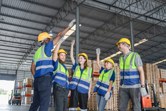 Diverse group of warehouse workers celebrating teamwork success with high five in storage facility, Teamwork celebration concept.