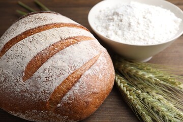 Fresh bread, flour and green wheat spikes on wooden table, closeup