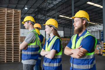 Group of multiethnic warehouse workers standing in confident pose with arms crossed, wearing safety vests and helmets in organized storage facility