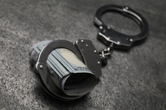 Corruption. Handcuffs and dollar bills on grey table, closeup - Powered by Adobe