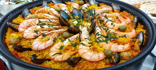 A large bowl of seafood paella with shrimp, mussels, and olives. The dish is colorful and...