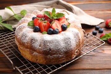 Tasty Bundt cake with powdered sugar and berries on wooden table, closeup
