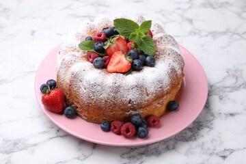 Tasty Bundt cake with powdered sugar and berries on white marble table, closeup