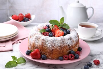 Tasty Bundt cake with powdered sugar and berries on white marble table, closeup