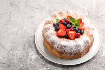 Tasty Bundt cake with powdered sugar and berries on grey textured table, space for text