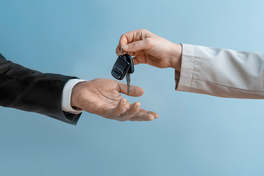 Woman's hand  handing over car keys to a man's hand in a formal suit. Concept of selling or renting a car