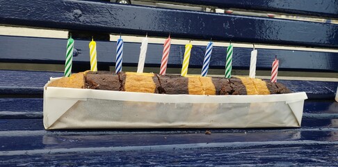 A tray of assorted brownies and cookies sits on a bench with candles lit on top. The candles are in...