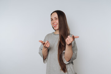 A young woman with long brown hair wearing a gray t-shirt, smiling and pointing playfully at the...