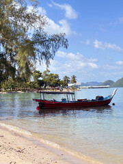 A vibrant red boat floats peacefully on clear turquoise waters beside a sandy beach, framed by lush green trees under a bright blue sky.