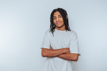 Young man with braided hair in a white t-shirt, arms crossed, smiling.