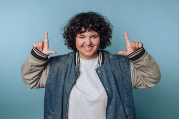 A person with curly hair wearing a denim jacket and white t-shirt smiles while making a playful...