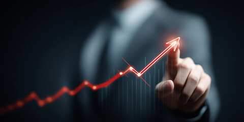 Person in suit is pointing at glowing red upward trend line on virtual graph, symbolizing business growth and success. background is dark, highlighting graph vibrant color