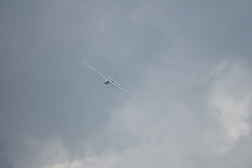 Training glider taking a tight turn on final approach to landing. Head-on view against an overcast sky.