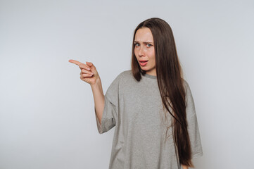 A woman with long hair in a gray t-shirt pointing to the side with a surprised expression.